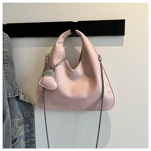 Detail of pink pleated clutch bag with silver chain strap and heart charm on white wall
