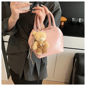 Pink glossy leather shoulder bag with bear pendant and embossed letters in a cafe setting