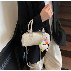 Detailed shot of cream bowling bag with plush charm and adjustable strap on stairs