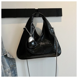 Detail of black glossy pleated handbag featuring silver heart charm and metal chain