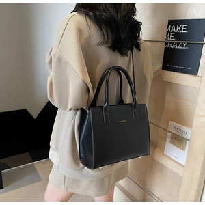 Detail of black faux leather tote with gold brand name and adjustable shoulder strap