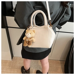 Detail showing cream white textured leather handbag with a plush bear charm on the side