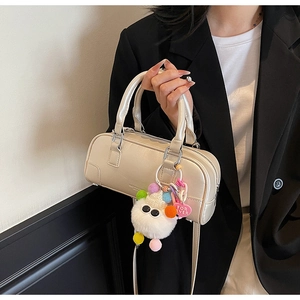 Close-up of cream bowling bag featuring a plush monster charm with a heart-shaped tag