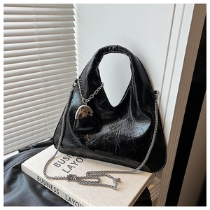 Close-up of black glossy wrinkled hobo bag with silver chain and heart charm detail