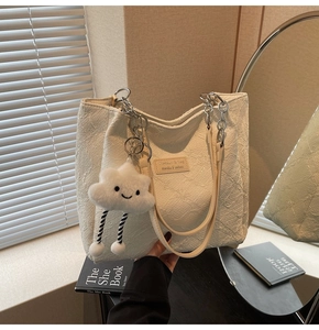 Detail of cream tote bag with textured fabric, metal chain strap and cloud plush charm