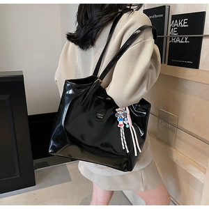 Back view of model wearing a large black glossy leather tote bag with gold logo
