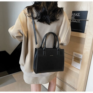 Detail of elegant black leather handbag with gold logo shown on model's shoulder