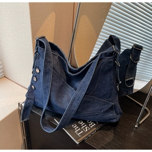 Detail of dark blue denim tote bag showing silver metal buckles and shoulder strap