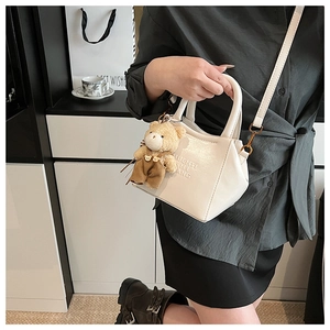 Chic white glossy shoulder bag with a teddy bear pendant shown in a lifestyle setting