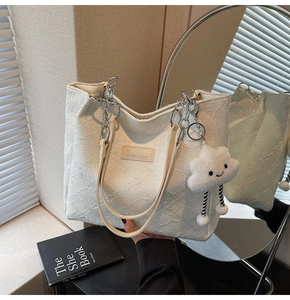 Detail of off-white tote bag with embossed texture, silver chain strap, and cloud charm