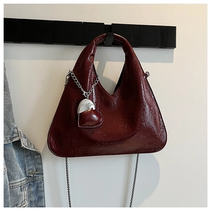 Detail of burgundy patent leather bag with heart charm and silver chain strap