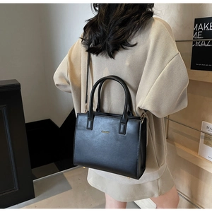 Detail of a black leather crossbody tote bag featuring elegant golden logo lettering