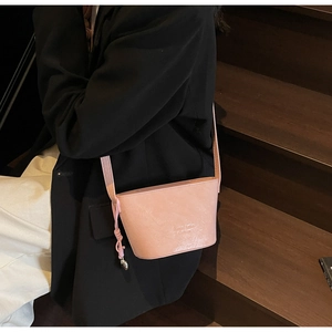 Sac seau en cuir rose avec logo embossé porté par un mannequin dans un escalier