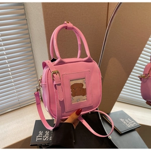 Detail of pink patent leather handbag featuring clear card slot and golden hardware