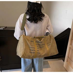 Detail of a large khaki canvas travel duffel with green shoulder strap and yellow leather accents