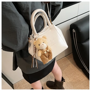 Detail of white leather shoulder bag featuring a cute teddy bear charm and textured finish