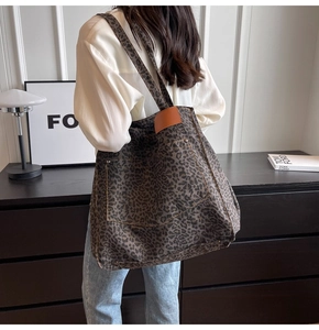 Detail of leopard print canvas tote bag with outer pocket and leather handles on model