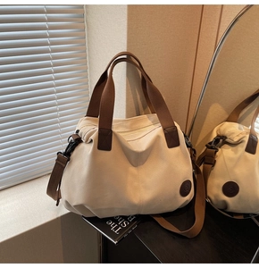 Close-up of cream canvas travel bag with brown textile handles and leather logo patch