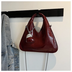 Detail of burgundy wrinkled patent leather handbag with silver chain and heart charm