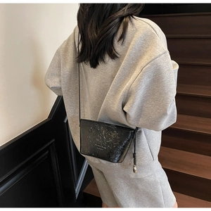 Détail du sac seau noir brillant avec texture gaufrée et logo métallique Fashion sur le rabat
