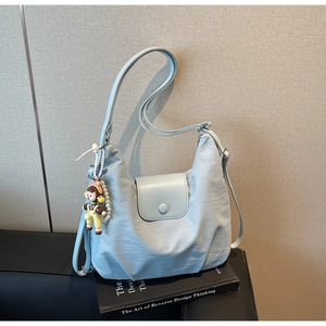 Detail of light blue canvas tote bag with snap closure and pearl doll charm accessory