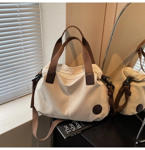 Detail of travel tote bag with brown straps and round leather logo patch on beige canvas