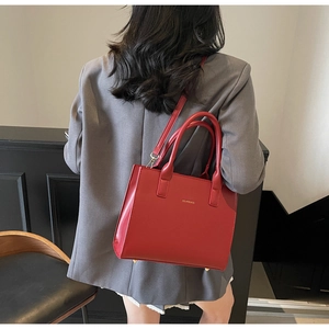 Detail of red minimalist tote bag featuring golden protective feet and branding logo