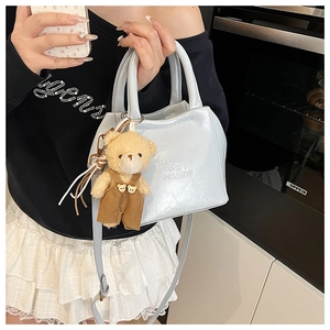 Detail view of light blue textured shoulder bag with cute plush bear charm accessory