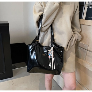 Close-up of black patent leather tote bag with cartoon charm and tassel detail