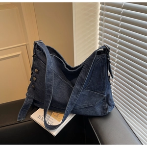 Close-up of vintage blue denim tote bag with decorative metal buttons on a leather sofa