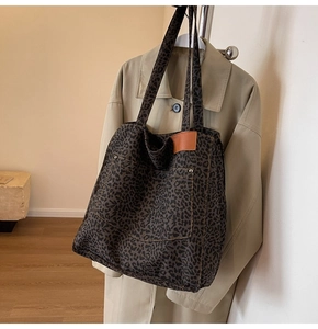 Detail of leopard print canvas tote bag with leather patch and rivet accents hanging with trench coat