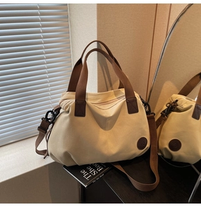 Macro view of cream canvas tote bag with brown webbing handle and round leather logo