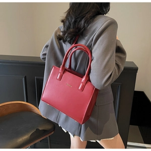 Detail of red leather tote bag with gold logo being carried by a model in a grey suit