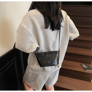 Gros plan d'un sac seau bandoulière en cuir plissé noir porté sur un sweat gris