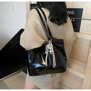 Close-up of black glossy patent leather tote bag with cute doll and tassel accessories