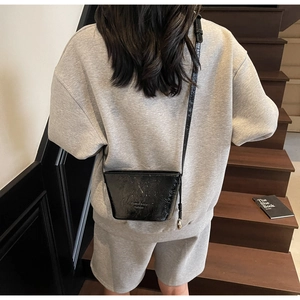 Détail d'un sac seau noir en cuir verni brillant porté avec une tenue décontractée