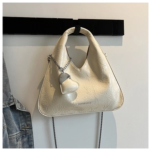 Detail of pleated cream crossbody bag featuring a gold chain and heart charm accessory