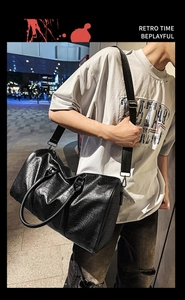 Close-up of black crocodile embossed travel bag with adjustable strap in urban setting