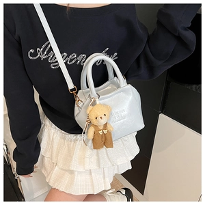 Detail of light blue patent leather handbag with embossed text and cute bear charm