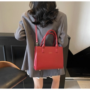 Detailed view of structured red leather handbag featuring gold logo and twin top handles