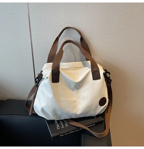 Detail of a large canvas travel bag with brown straps on a black leather sofa