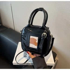 Detail of black patent leather handbag featuring a round handle and puppy decor card slot