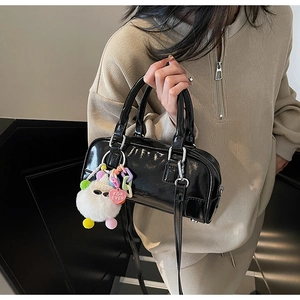 Detail of black patent leather bowling bag with a cute plush doll charm and zipper closure
