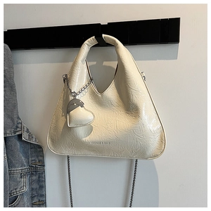 Detail of cream pleated crossbody bag with heart pendant and metal chain strap
