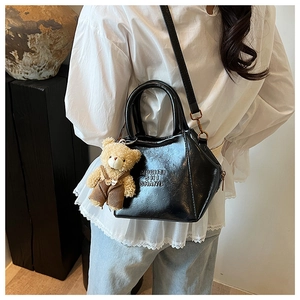 Detail of black glossy leather tote bag with a cute plush bear charm and gold hardware