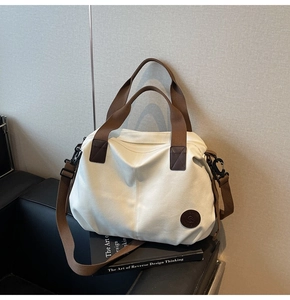 Detail of white canvas tote bag with brown leather logo patch on a black sofa