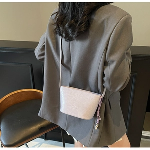 Détail du sac seau violet clair à texture plissée porté sur un blazer gris chic