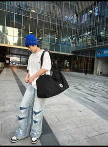 Macro view of large black nylon tote bag with durable side logo and adjustable strap