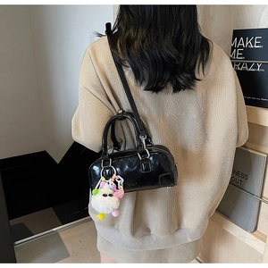 Detail of black patent leather bowling bag with cute cat plush charm on female model
