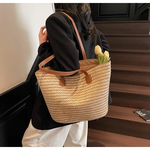 Detail of the woven straw tote bag texture and brown leather strap on model